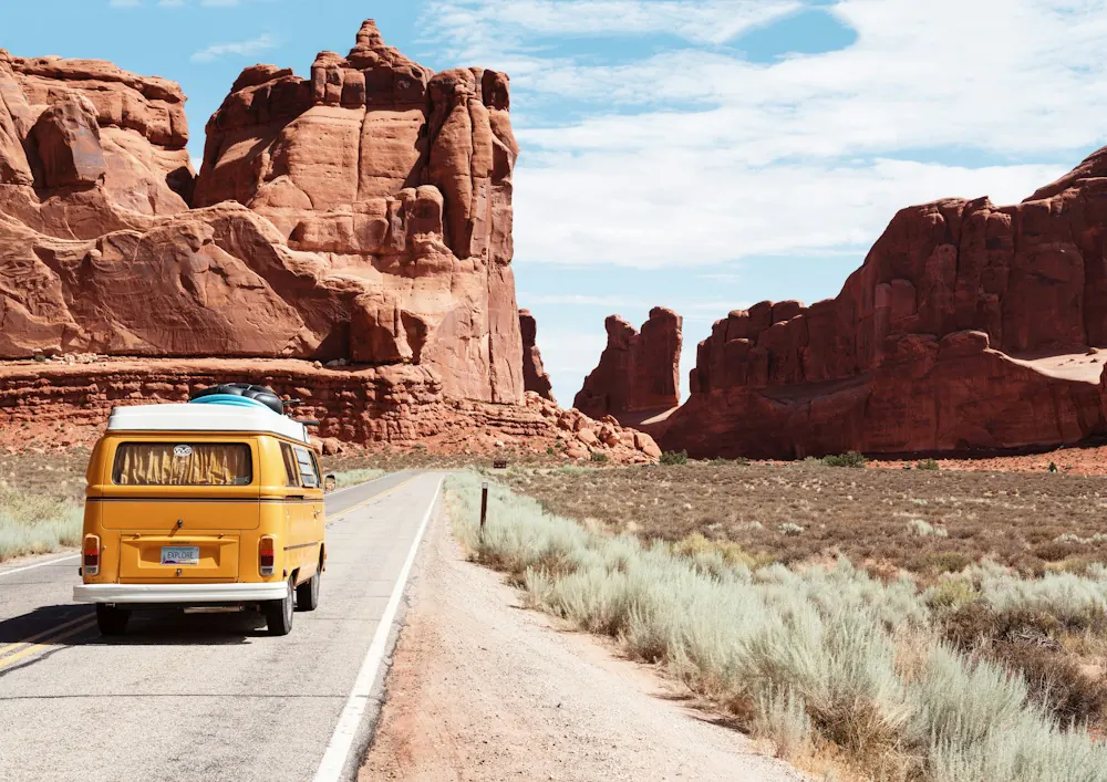 Yellow camper van on a desert road past red rocks