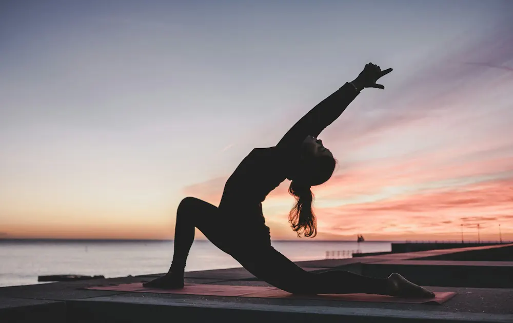Person doing yoga on the beach at sunset